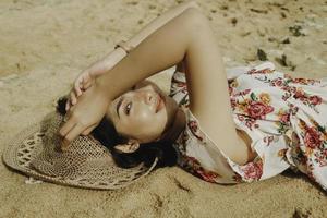 een jonge mooie Aziatische vrouw verblind door het licht terwijl ze op het strandzand ligt foto