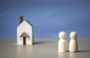 twee houten figuren van mensen met geluk en een huis op blauwe achtergrond. betaalbare woningen en hypotheken voor het kopen van concept jonge gezinnen en koppels. familie nest en kopieer ruimte. foto