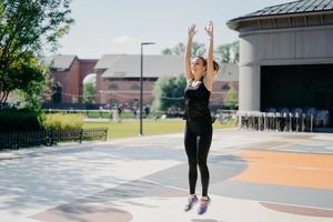 positief actief vrouwelijk model heeft cardiotraining buitenshuis springt hoog houdt armen omhoog gekleed in activewear sterk fit besteedt vrije tijd in het stadion heeft regelmatig ochtendtraining. fitness en sport foto