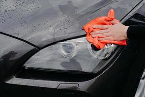 mans hand met vod afvegende auto's koplamp. natte zwarte auto reinigt bij wasstraat. autoreinigings- en serviceconcept foto