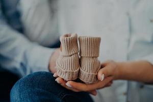 onherkenbare vrouw en man anticiperen op baby houdt kleine slofjes vast. familie moederschap vaderschap concept. toekomstige ouders. geboorte foto