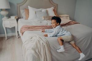 vrolijke kleine Afro-Amerikaanse jongen die binnenshuis op bed geniet van speeltijd foto