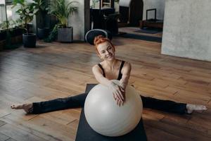 lachende gember gezonde vrouw in gespleten positie die zich uitstrekt met fitball foto