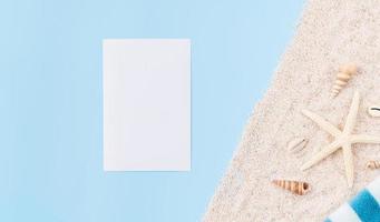 bovenaanzicht van blanco papier voor reclameborden met zeester en handdoek op zand, blauwe achtergrond. zomertijd concept. foto
