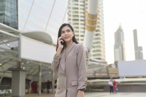 een jonge, mooie zakenvrouw gebruikt een smartphone in de moderne stad, bedrijfstechnologie, stadslevensstijlconcept foto