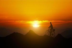 leiderschap en doelen. een man die op de top van een berg op een fiets staat en naar de zonsondergang kijkt. conceptuele afbeelding composiet. foto