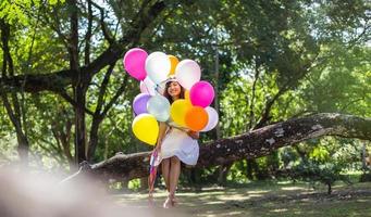 jong tienermeisje zittend op een boom en ballonnen in de hand houdend foto