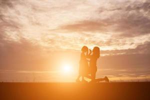een silhouet van een gelukkig jong meisje kind de armen van zijn liefhebbende moeder voor een knuffel, voor de zonsondergang aan de hemel op een zomerdag. foto