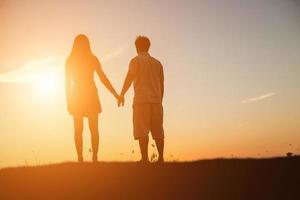 silhouet van een man en vrouw hand in hand met elkaar, samen wandelen. foto