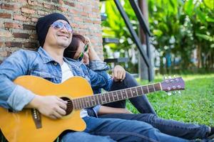 hipster man gitaar spelen voor zijn vriendin buiten tegen bakstenen muur, samen genieten. foto