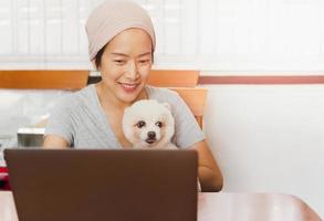 Kaukasische freelancer-vrouw die haar Pommerse hond vasthoudt terwijl ze thuis op een laptop werkt. foto