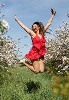 jonge blanke vrouw in rode jurk genieten van de bloei van een appelbomen, springen foto