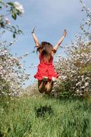 jonge blanke vrouw in rode jurk genieten van de bloei van een appelbomen, springen foto