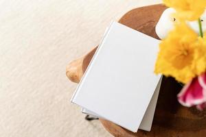 wit boek blanco omslagmodel op stijlvolle houten salontafel met tulpenboeket, hoge hoekweergave foto