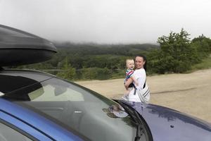 een mooie vrouw en haar zoontje omhelzen elkaar stevig tegen de achtergrond van een bergmeer hoog in de bergen en een auto met een imperiaal. reizen met kinderen. foto