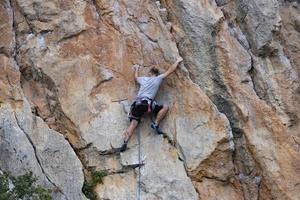 een man, een atleet, een bergbeklimmer op een steile rode rots. het concept van actieve, extreme recreatie en hobby's. uitzicht vanaf de achterkant. foto