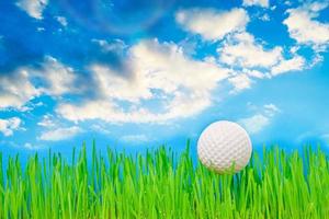 golfbal op een groen gazon tegen een blauwe lucht met wolken. foto
