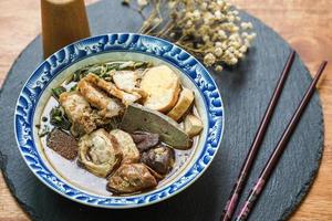 gerolde rijstnoedels in vijfkruidenbouillon geserveerd in een betegelde beker op een houten tafel. foto