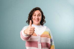 lachende Spaanse jonge vrouw duimen opdagen op blauwe achtergrond foto