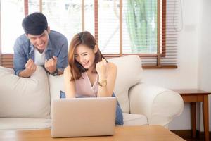 mooi portret Aziatische jonge paar werkende laptop met glimlach en gelukkig zittend op de bank in de woonkamer, man en vrouw op de bank met behulp van notebookcomputer met opgewonden, zakelijke en succes concept. foto