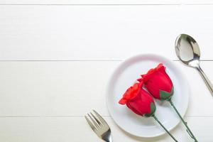 cadeau met rood roze bloem en schotel en lepel en vork op houten tafel, 14 februari van liefdesdag met romantische kopieerruimte, valentijn vakantieconcept, bovenaanzicht. foto