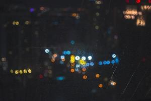 waterdruppels op raam met bokeh lichte achtergrond van het nachtelijke uitzicht op de stad foto