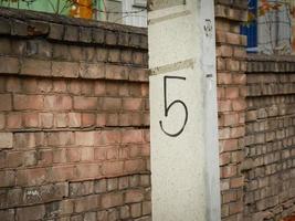 nummer vijf handgeschreven in zwarte verf op betonnen paal buiten in de buurt van bruine bakstenen muuromheining foto