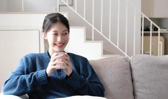 portret van lachende gelukkig vrolijke mooie mooie Aziatische vrouw ontspannend drankje. meisje kappen geniet van het ontbijt in de vakantie ochtendvakantie op de bank thuis foto