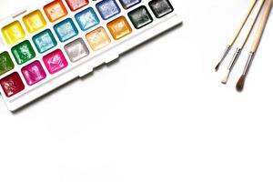 een palet van achttien kleuren aquarellen en penselen op een witte achtergrond met ruimte voor tekst. foto