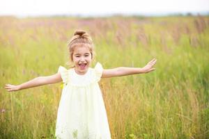 het meisje rent het veld in met haar armen gestrekt als een vliegtuig. zorgeloze jeugd, zomer vrijheid, reizen. internationale kinderdag. muggenspray, cottage core. foto