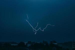bliksem in de lucht boven de stad. heldere flitsen op donkere nacht. onweerswolken en elektriciteitsontladingen in de atmosfeer. foto