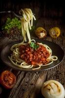 spaghetti pasta, tomatensaus op een zwarte plaat ziet er heerlijk uit op een oude houten tafel, zwarte achtergrond. foto