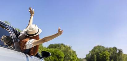 vrouw stak haar handen in de lucht en uit de auto met plezier en geluk voor solo road trip zomervakantie en weekend reizen vrijheid concept met kopieerruimte foto