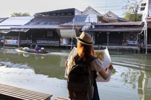 Aziatische vrouw reist naar Zuidoost-Azië, Thailand, terwijl ze een papieren kaart gebruikt om de bestemming te lokaliseren zonder mobiele telefoontoepassing om te genieten van de levensstijl van een vredige sfeer van een lokaal dorp foto