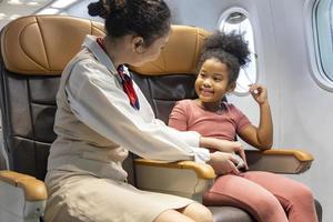 stewardess helpt de veiligheidsgordel vast te maken voor een klein afro-amerikaans kind na het instappen in het vliegtuig als veiligheidsprocedure voor het opstijgen foto