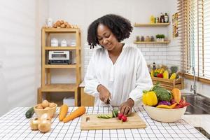 Afro-Amerikaanse huisvrouw hakt biologische komkommer om een eenvoudige en gemakkelijke salademaaltijd in zuidelijke stijl te bereiden voor een veganistisch en vegetarisch voedselconcept foto