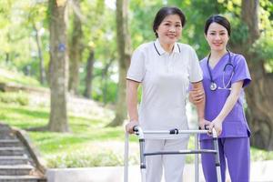 Aziatische vrouwelijke verpleegster die voor een vrouwelijke patiënt van middelbare leeftijd in het park zorgt foto
