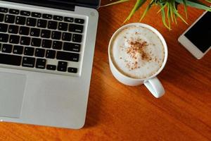 hete latte in beker op houten tafel uitzicht van bovenaf met laptop en smartphone rond. foto