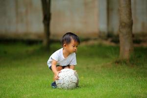 Aziatische jongen voetballen in het park. kind met bal in grasveld. foto