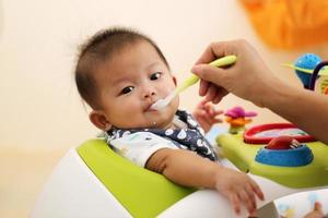 moederhanden die voedsel voor aziatische baby voeden. jongen aan het eten. foto