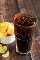 een glas iced cola met chips op houten tafel. frisdranken en chips. foto