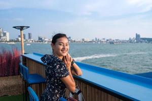 aantrekkelijke gelukkige aziatische vrouw zit aan de tafelbar drijvend op zee met uitzicht op de stad foto