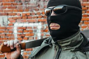 commando in een masker en bril met een machete in zijn hand tegen een bakstenen muur foto