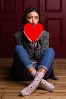 kortharige vrouw in jasje met lippen die kus vormen, zittend op de vloer, benen gekruist met hartvorm voor haar kin foto
