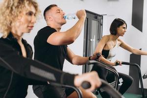 jonge man drinkwater en vrouwen met behulp van luchtfiets voor cardiotraining bij cross training gym foto