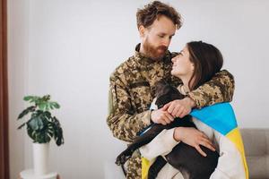 een oekraïens stel, een soldaat in militair uniform en een meisje gewikkeld in een oekraïense vlag houden een hond in hun armen, gelukkig samen. foto