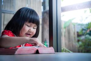 klein meisje dat thuis de bijbel leest, het pure geloof van het kind foto