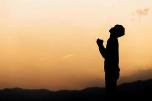 silhouet van een man hand in hand en gebed op de berg bij zonsondergang. begrip religie. foto