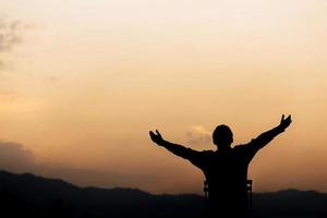 silhouet van een man handen omhoog en gebed en aanbidding god bij zonsondergang. begrip religie. foto