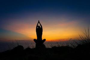 silhouet van een vrouw die krijger één pose yoga beoefent op het strand bij zonsondergang foto